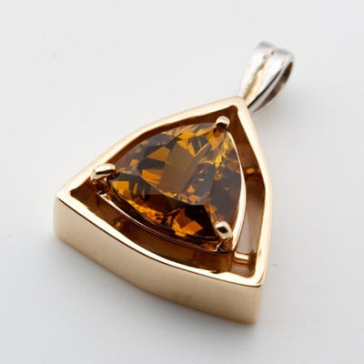 Gold-trimmed pendant with a triangular cut gemstone on a white background