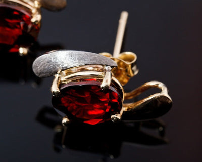 Gold earring with a red gemstone on a dark background